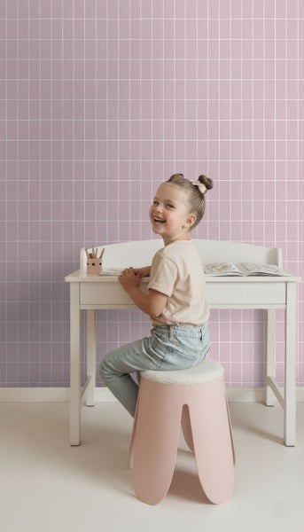 Mädchen sitzt an Schreibtisch vor Tapete mit Fliesendesign