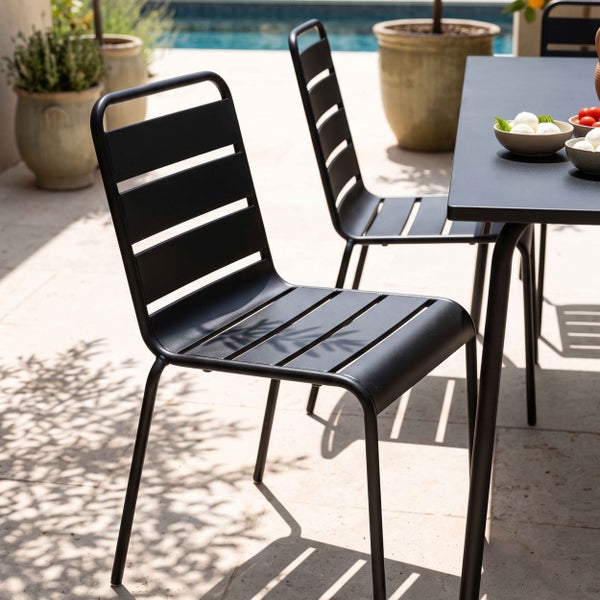 Moderner schwarzer Stapelstuhl aus Metall mit Lamellendesign in einer hellen und organisierten Terrassenatmosphäre neben einem Gartentisch.