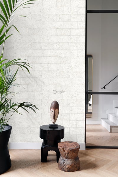 Szene mit Wandpaneelen in Steinoptik, einer Zimmerpflanze, einem dekorativen Hocker und einer Maske