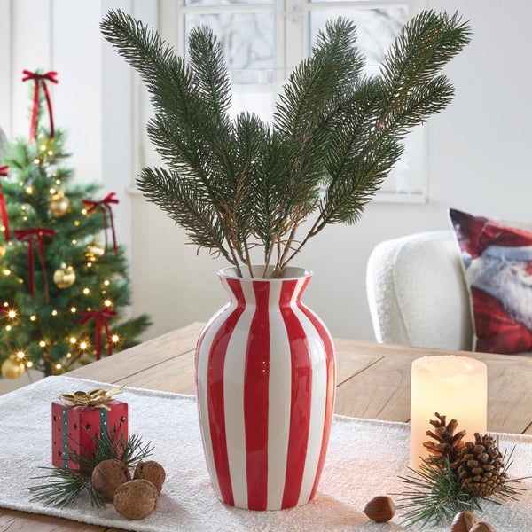 Weihnachtliche Tischdekoration mit einer gestreiften Keramikvase gefüllt mit Tannen Zweigen auf einem Tisch mit Kerze und Geschenken.