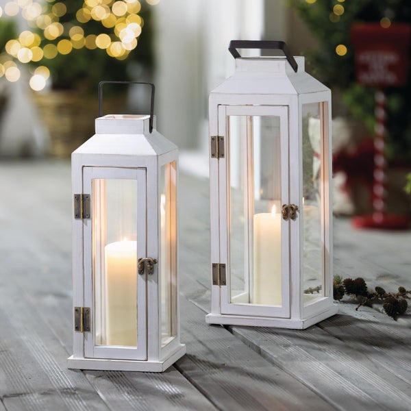 Zwei dekorative Windlichter aus Holz mit Glasfenstern und Kerzen auf einem Holzboden in weihnachtlicher Umgebung.