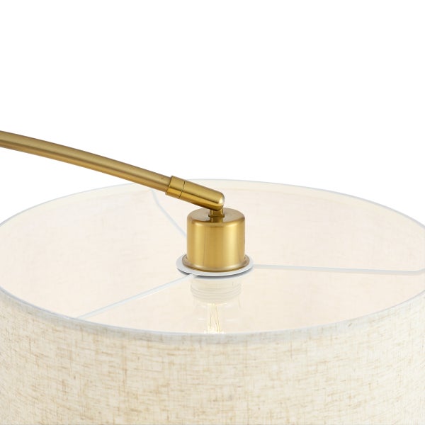 Detailansicht eines runden Lampenschirms aus hellem Textil mit einem messingfarbenen Metallgelenk und sichtbarem Leuchtmittel.