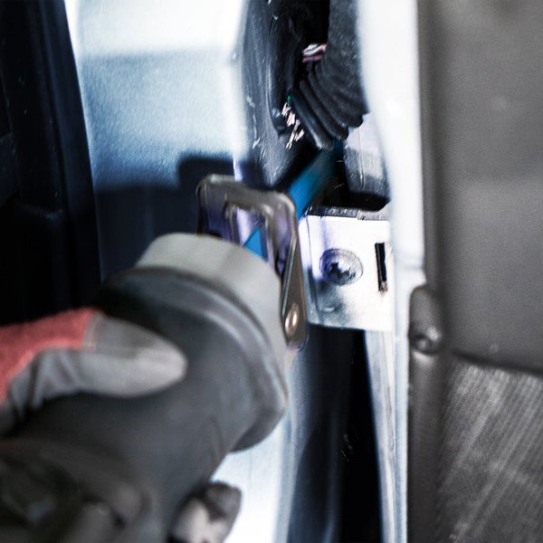 Handwerker demontiert mit Werkzeug ein Bauteil im Fahrzeug.