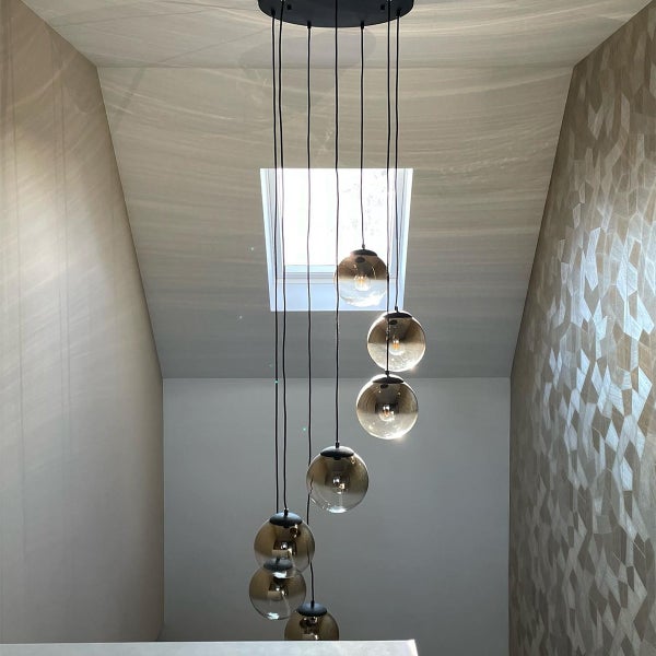 Hängelampe mit mehreren Glaskugeln im Treppenhaus unter einem Dachfenster.