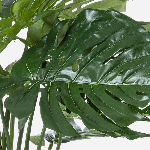 Künstliches grünes Blatt einer Monstera mit charakteristischen Schlitzen und Löchern, glänzende Oberfläche, sichtbare Adern.