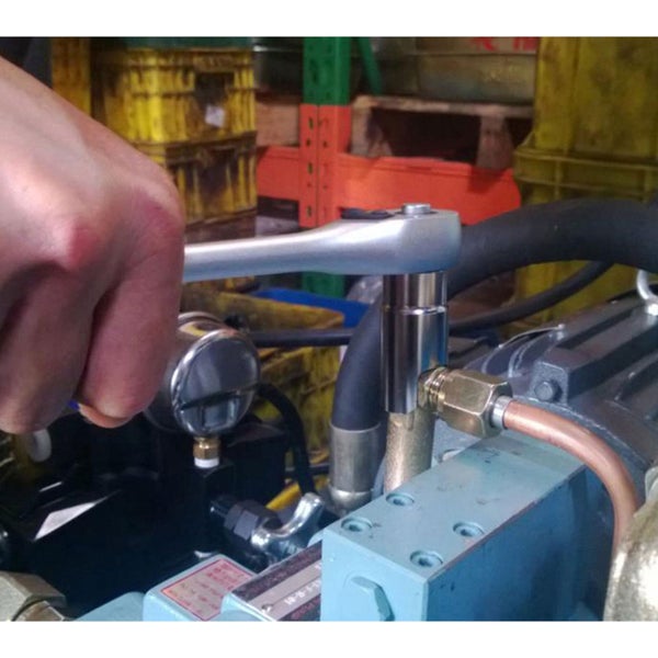 Hand nutzt eine Ratsche mit Steckschlüsseleinsatz an einem Maschinenteil mit Druckmanometer und Kupferleitung.