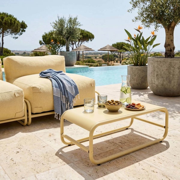 Moderner Lounge-Bereich auf einer Terrasse am Pool mit beigen Loungesesseln, einem Metall-Couchtisch und Pflanzen in großen Kübeln.