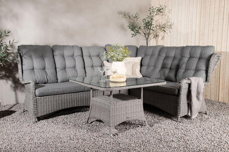 Gartenszene mit grauer Rattan-Lounge-Ecke und Couchtisch mit Glasplatte