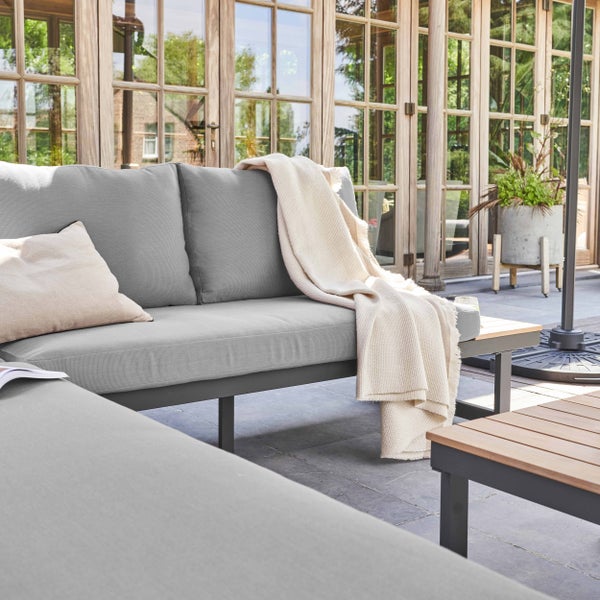 Moderne Gartenbank mit integriertem Holztisch und grauen Sitzkissen.