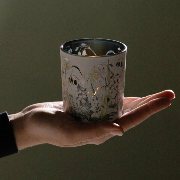 Ein Teelichthalter aus Glas mit floralem Blumenmuster, der in einer Hand gehalten wird.