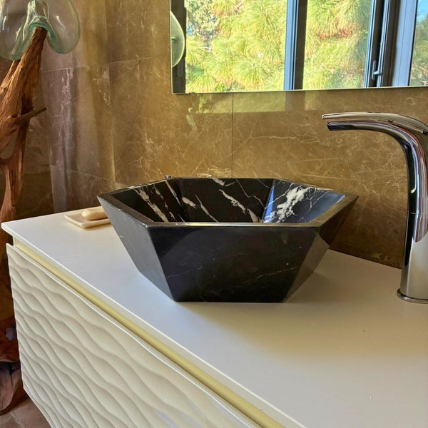 Sechseckiges Aufsatzwaschbecken aus schwarzem Marmor auf einem weißen Unterschrank in einem hellen, modernen Badezimmer.
