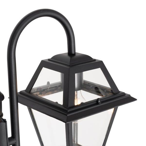Schwarze Außenwandleuchte im klassischen Laternendesign mit gebogenem Arm und klaren Glasscheiben mit brennendem Leuchtmittel.