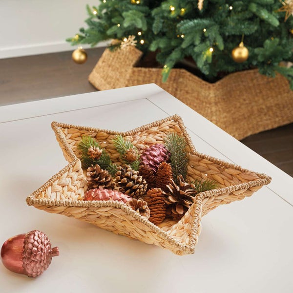 Dekoratives Arrangement mit Sternschale aus Naturfasern, Tannenzapfen und Weihnachtskugeln auf einem Tisch