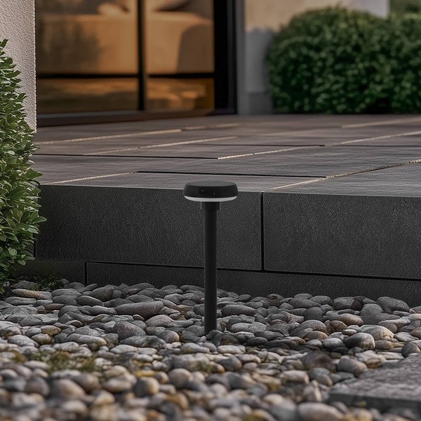 Schwarze LED-Außenleuchte mit Erdspieß in einem Kieselbeet neben einer modern gefliesten Terrasse.