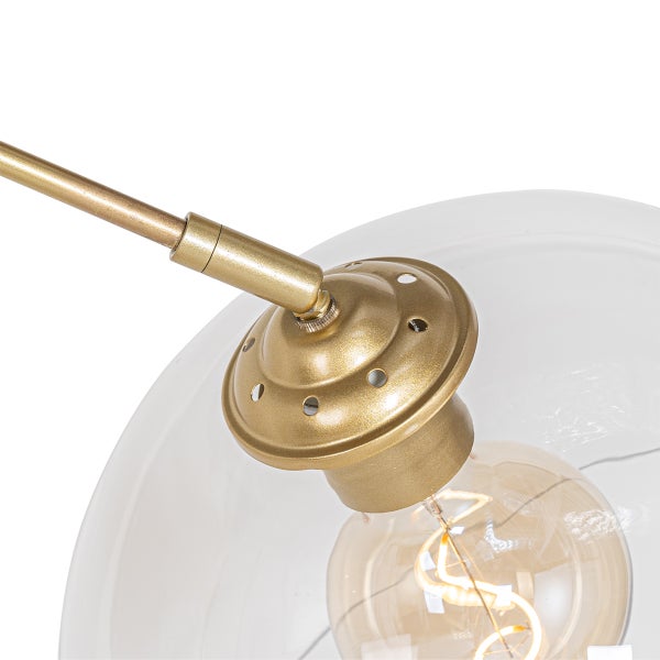Detail einer Pendelleuchte mit einem transparenten Glasschirm und einer goldenen Armatur