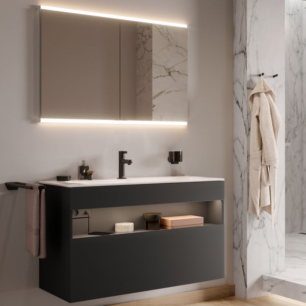 Modernes Badezimmer mit Waschtischunterschrank, Spiegelschrank mit Beleuchtung, schwarzer Armatur und Ablagefächern vor einer Marmorwand.