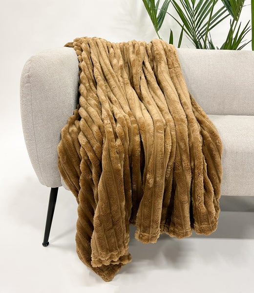 Ein beiger Plüschüberwurf liegt auf einem Sofa.