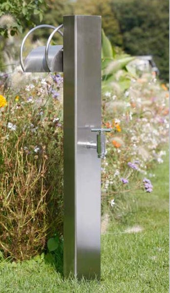 Garten-Wasserzapfstelle aus Edelstahl mit Wasserhahn und Schlauchhalter in einem hellen Garten mit Blumen und Gras.