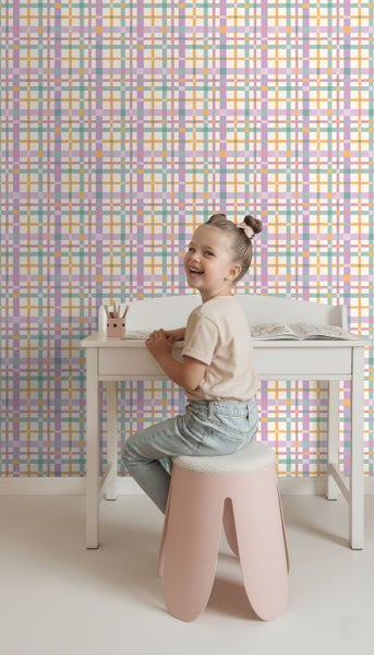 Vliestapete mit buntem Karomuster in einem hellen Kinderzimmer mit weißem Schreibtisch und rosa Hocker.