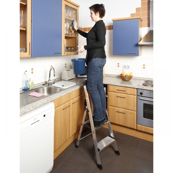 Frau reinigt Küchenschrank stehend auf einer Trittleiter