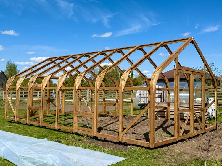Holzgerüst für ein Gewächshaus mit bogenförmigen Sparren auf einer Wiese, teilweise aufgebaut, Rahmenkonstruktion aus Holz für den Garten.