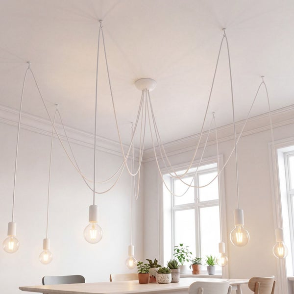 Weiße mehrflammige Pendelleuchte im Spinnen-Design über einem Esstisch in einem hellen, modernen Raum mit Pflanzen.