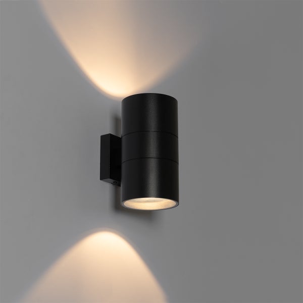 Zylindrische schwarze Wandleuchte mit Lichtaustritt nach oben und unten an einer Wand.