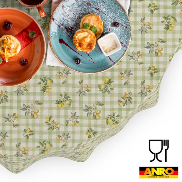 Abwaschbare Tischdecke mit grün-weißem Karomuster und Zitronenmotiv auf einem gedeckten Tisch mit Tellern und Speisen. Lebensmittelgeeignet. ANRO Logo.