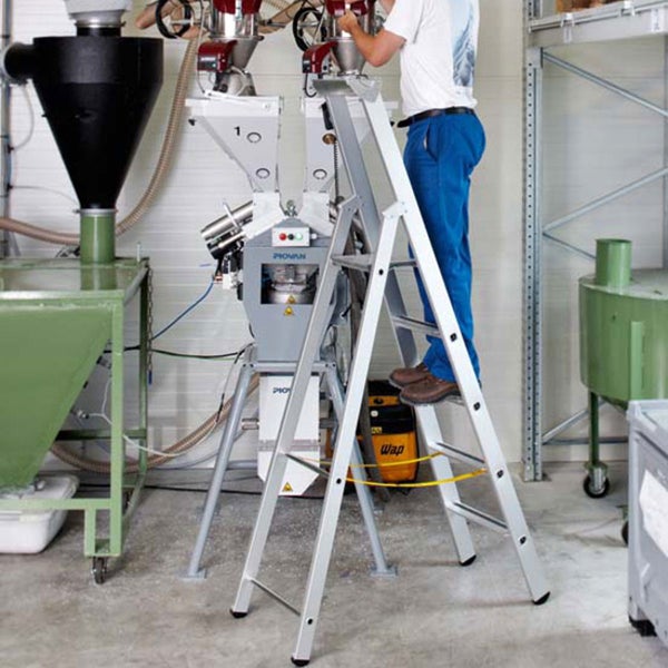 Mann auf einer Aluminiumleiter, der an einer Industriemaschine arbeitet