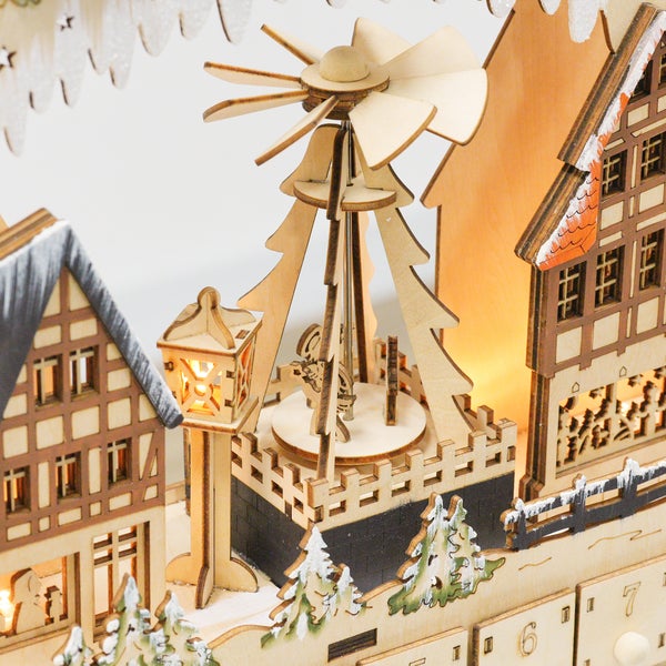 Detailansicht eines hölzernen Adventskalenders mit beleuchteten Fachwerkhäusern und einer kleinen Weihnachtspyramide.