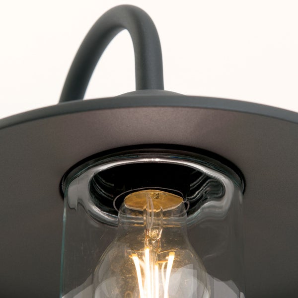Detailaufnahme einer Außenwandleuchte aus Metall mit flachem Schirm, schützendem Glaszylinder und brennendem Leuchtmittel.