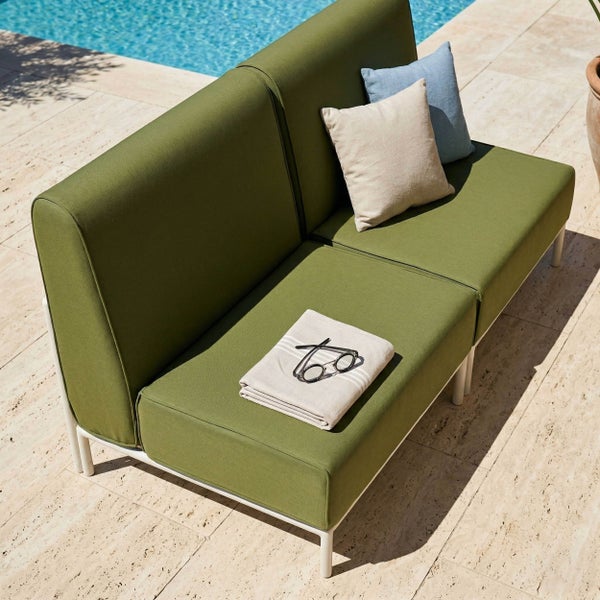 Modernes grünes Gartensofa mit weißem Metallgestell, dicken Polstern und Kissen auf einer Steinterrasse am Pool.