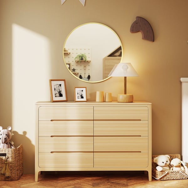 Kommode aus hellem Holz mit acht Schubladen in einem Kinderzimmer, darüber ein runder Wandspiegel, daneben geflochtene Körbe mit Kuscheltieren.