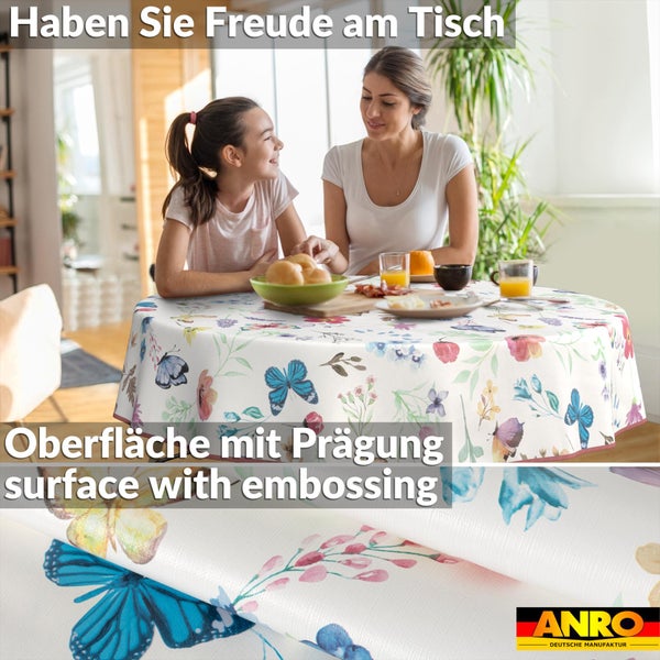 Runde Wachstischdecke mit Blumen- und Schmetterlingsmuster auf Tisch in hellem Raum. Nahaufnahme der Prägung. ANRO Logo.