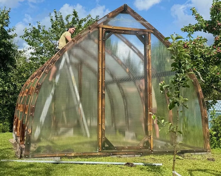 Gewächshaus aus Holz mit transparenten Platten und gebogenen Seitenwänden bei der Montage im Garten.