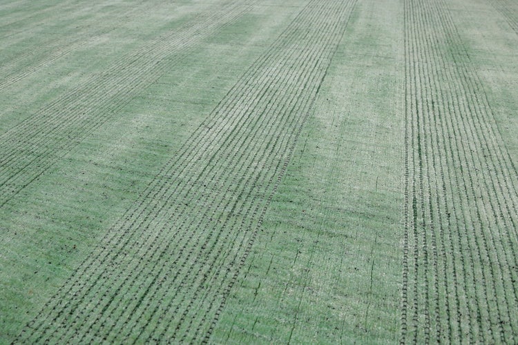 Grüner Kunstrasen mit Rippenstruktur und Drainage-Linien in der Nahaufnahme.