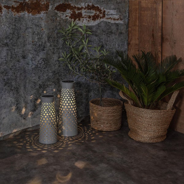 Dekorative Szene mit zwei Solarleuchten mit Muster, Olivenbaum und Zylinderpalmfarn in Pflanzkörben