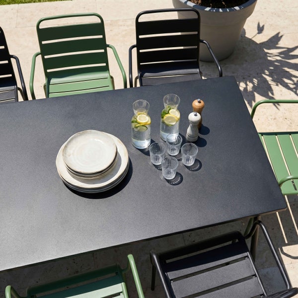 Moderner Gartentisch aus Metall mit Armlehnenstühlen auf einer Terrasse, gedeckt mit Tellern, Glaskaraffen und Gläsern in heller Atmosphäre.