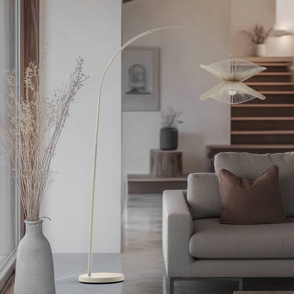 Innenaufnahme eines Wohnzimmers mit einer Bogenlampe aus Metall und einem Lampenschirm mit geometrischen Mustern neben einem Sofa