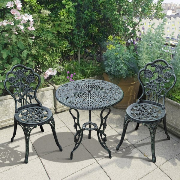 Dreiteiliges Garten Bistro Set mit rundem Tisch und zwei Stühlen aus Aluguss im Rosendesign auf einer Terrasse mit Pflanzen.