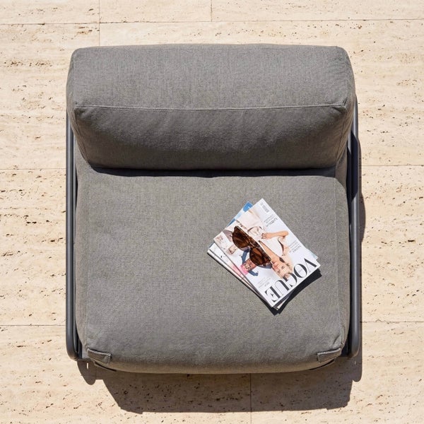 Grauer Garten-Lounge-Sessel mit Stoffpolsterung von oben gesehen, mit Zeitschriften und Sonnenbrille auf der Sitzfläche.
