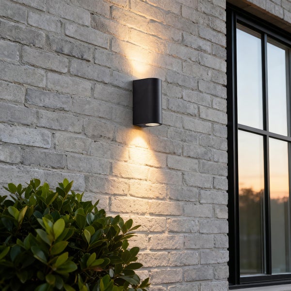 Moderne schwarze Außenwandleuchte mit Lichtaustritt nach oben und unten an einer Ziegelwand neben einem Fenster.