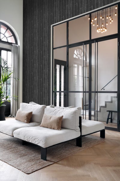 Wohnzimmer mit Couch, Teppich und Blick durch eine Glastür auf ein Treppenhaus