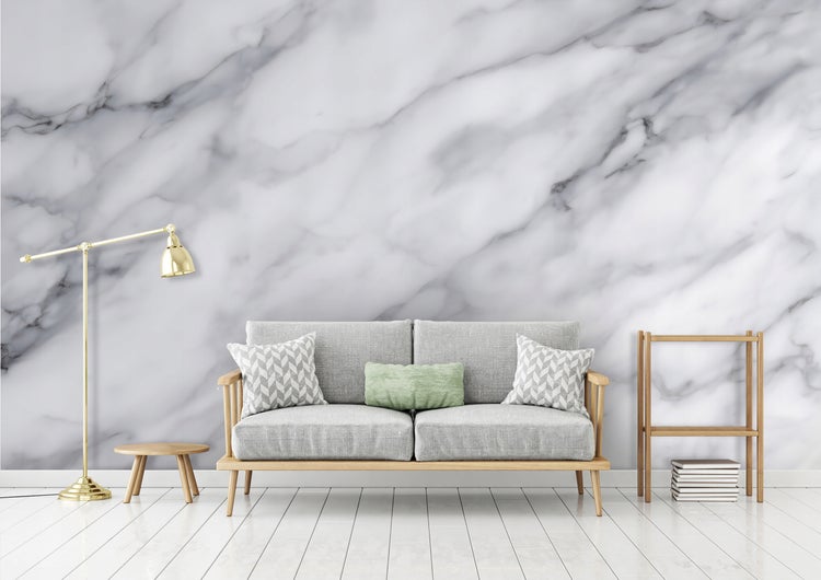 Helles Wohnzimmer mit Sofa, Stehlampe und Regal vor einer Marmorwand