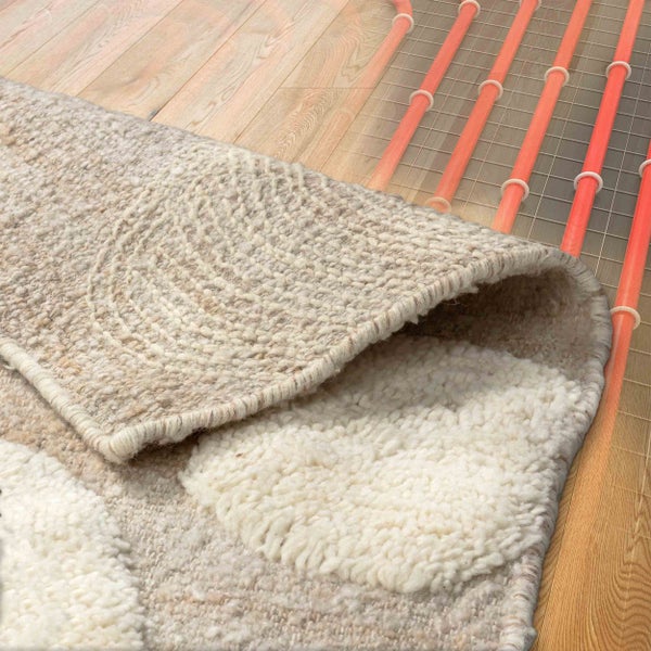 Wollteppich über einer Fußbodenheizung auf Holzboden, Heizrohre unter dem Teppich sichtbar.