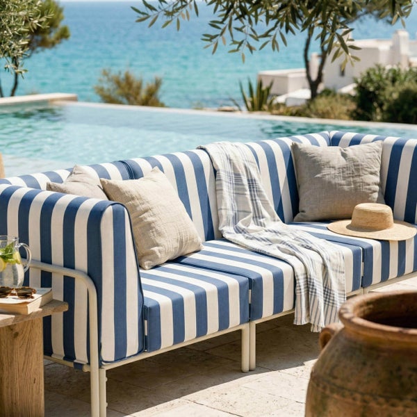 Garten-Loungesofa mit blau-weiß gestreiften Polstern und weißem Metallrahmen auf einer hellen Steinterrasse mit Pool und Meerblick.