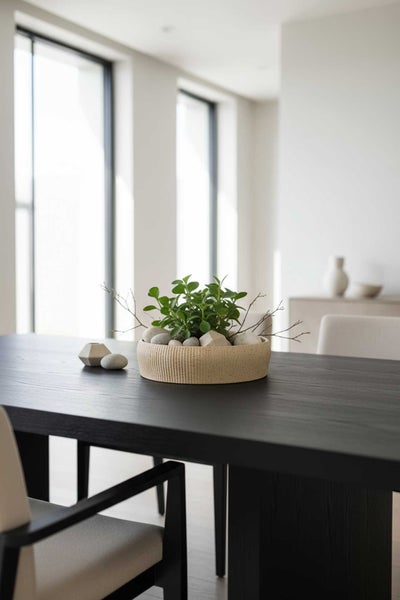 Moderne Dekoschale auf einem dunklen Holztisch mit grüner Pflanze, Steinen und Zweigen in einem hellen, minimalistischen Raum.