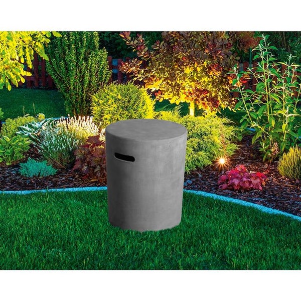 Zylindrischer Gartenhocker in Beton-Optik mit Griffmulde auf einer Rasenfläche in einem Garten mit Pflanzen.
