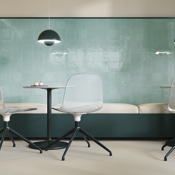 Moderne Wandgestaltung mit quadratischen Fliesen in glänzender Optik hinter einer Sitzbank mit transparenten Stühlen und runden Tischen.