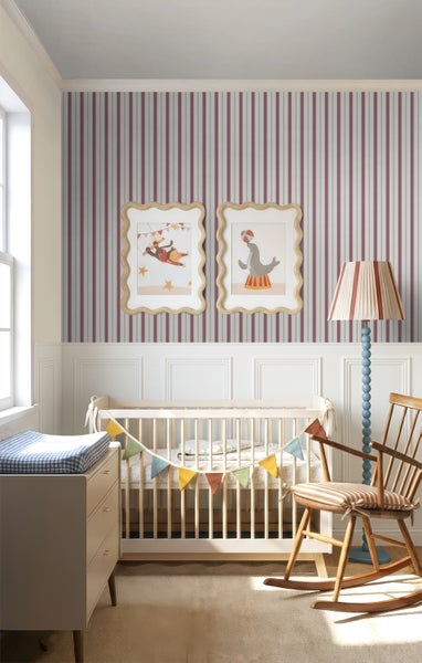 Helles Kinderzimmer mit gestreifter Tapete, weißer Wandvertäfelung, hölzernem Babybett, Wickeltisch und Schaukelstuhl im verspielten Zirkus-Stil.